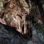 A cave interior featuring stalactites and stalagmites illuminated by multicolored lights.