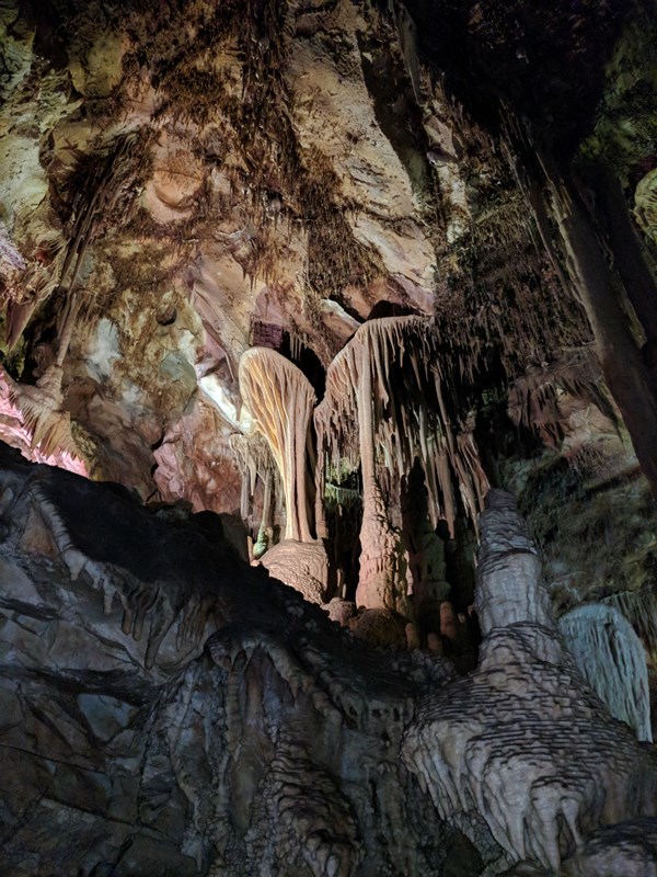 A cave interior featuring stalactites and stalagmites illuminated by multicolored lights.